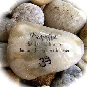 Op de afbeelding: Een lichtbruine steen met de woorden "Namaste the light within me honors the light within you" en het Om-symbool erop gegraveerd.