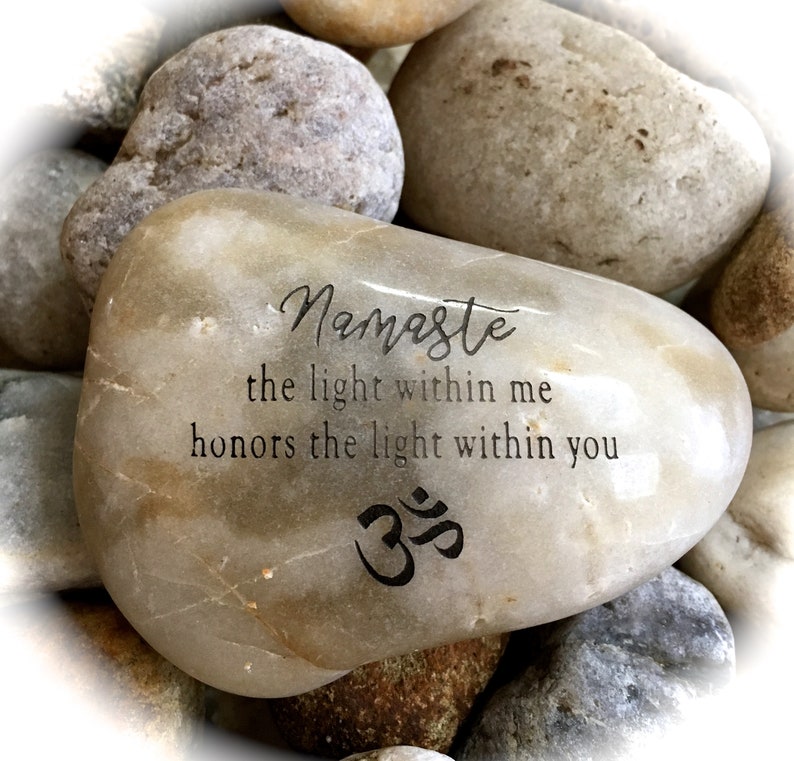 Op de afbeelding: Een lichtbruine steen met de woorden "Namaste the light within me honors the light within you" en het Om-symbool erop gegraveerd.