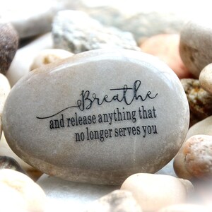 May include: A gray stone with the words "Breathe and release anything that no longer serves you" engraved on it.