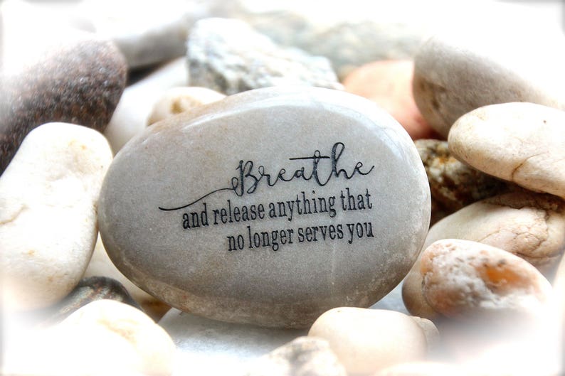 May include: A gray stone with the words "Breathe and release anything that no longer serves you" engraved on it.