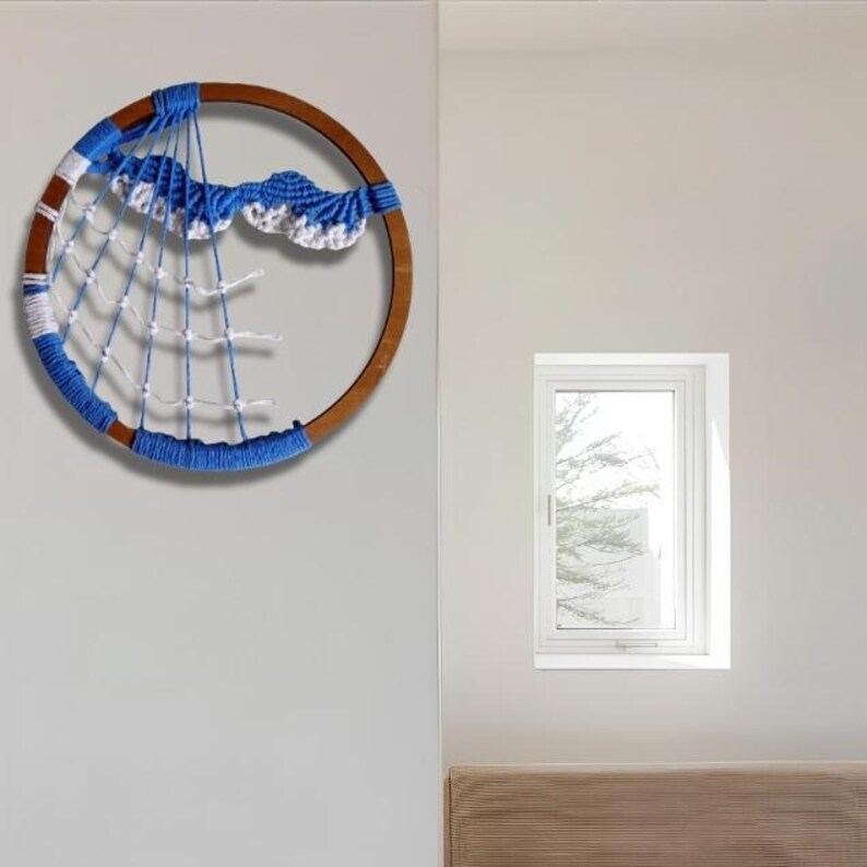 以下が含まれることがあります： 木製のフープに青と白の糸で飾られた手作りのドリームキャッチャー。デザインは、青いかぎ針編みの雲と白い糸のウェブを特徴とし、装飾的な壁掛けを作成します。ドリームキャッチャーはニュートラルな壁に展示されています。