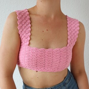 Op de afbeelding: Een roze gecrochete crop top met een vierkante halslijn en gegolfde randen.