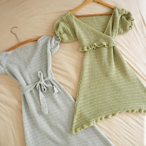 May include: Two crocheted dresses, one light green and one light blue, hanging on hangers. Both dresses have a V-neckline and short sleeves.