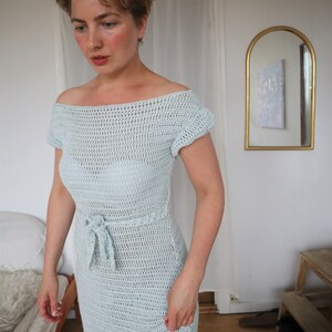 May include: A light blue crochet dress with a tie at the waist. The dress has a loose, off-the-shoulder neckline and short sleeves.