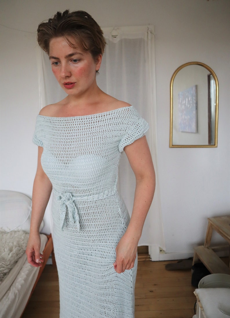 May include: A light blue crochet dress with a tie at the waist. The dress has a loose, off-the-shoulder neckline and short sleeves.