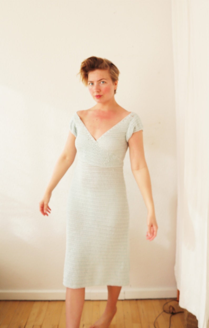May include: A woman wearing a light blue crochet dress with a V-neckline and short sleeves.
