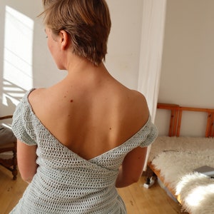 May include: A light blue crochet top with a deep V-neck and short sleeves. The top is made of a delicate, open-weave fabric.