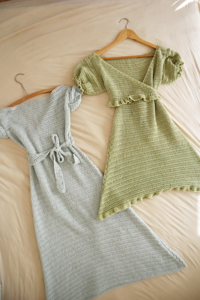 May include: Two crocheted dresses, one light green and one light blue, hanging on hangers. Both dresses have a V-neckline and short sleeves.
