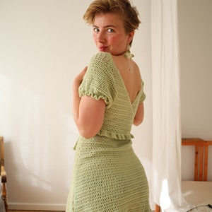 May include: A light green crochet dress with a ruffled hem and short sleeves. The dress is fitted and has a V-neckline.