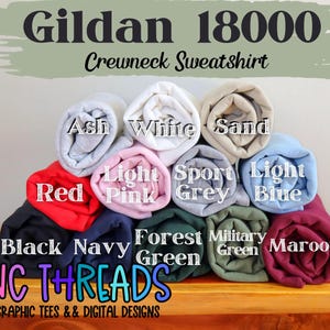 Puede incluir: Una pila de sudaderas con cuello redondo Gildan 18000 en varios colores, incluyendo rojo, negro, azul marino, verde bosque, verde militar, granate, ceniza, blanco, arena, rosa claro, gris deportivo y azul claro. El texto "NC THREADS" es visible en la parte inferior de la imagen.