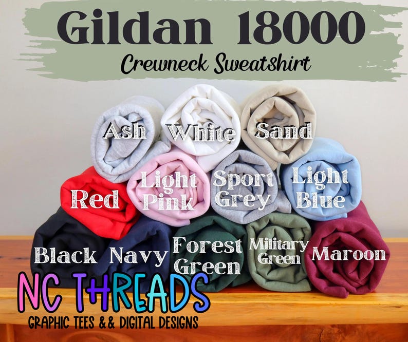 Puede incluir: Una pila de sudaderas con cuello redondo Gildan 18000 en varios colores, incluyendo rojo, negro, azul marino, verde bosque, verde militar, granate, ceniza, blanco, arena, rosa claro, gris deportivo y azul claro. El texto "NC THREADS" es visible en la parte inferior de la imagen.