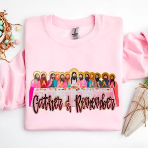 Puede incluir: Sudadera rosa con una ilustración colorida de la Última Cena y el texto "Gather & Remember".