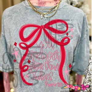 May include: A grey acid wash t-shirt with a large red bow design and the text "You are worth more than rubies" in pink script. The shirt also features the Bible verse Proverbs 3:10. The shirt is from NC Threads.