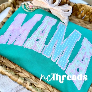 May include: Teal t-shirt featuring the word "NANA" in large, decorative letters. The letters are a mix of pink floral and blue polka dot patterns, outlined in pink. The brand name "ncThreads" is printed in white at the bottom.