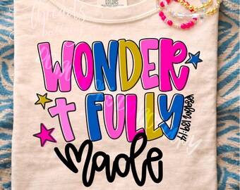 Puede incluir: Una camiseta color crema con el texto WONDER FULLY MADE en letras de burbuja coloridas en rosa, azul y amarillo. El diseño incluye pequeñas estrellas y el texto Psalm 139:14. Una pila de pulseras de cuentas coloridas descansa en el cuello.