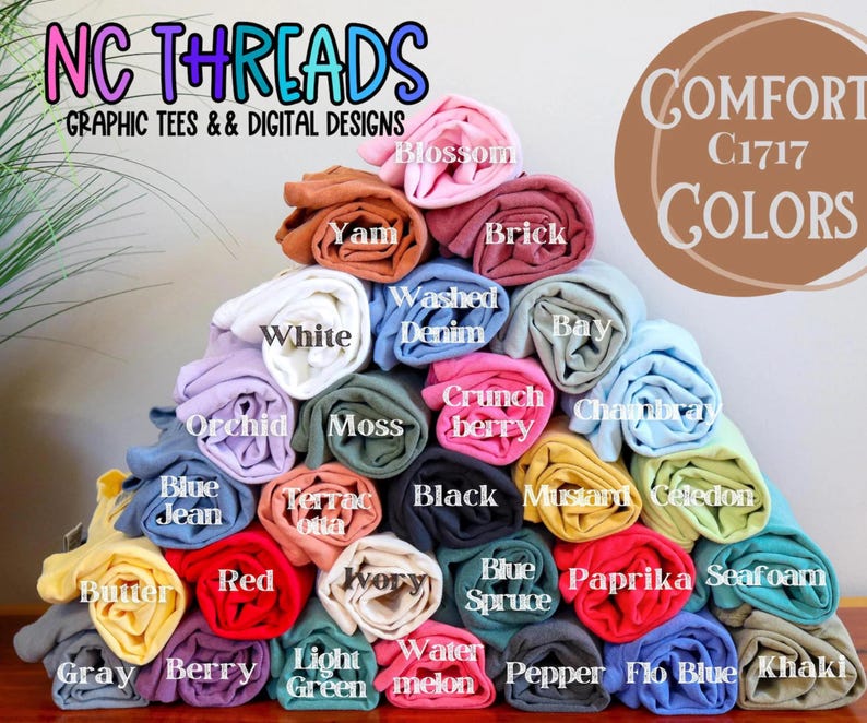 May include: A display of rolled-up t-shirts in various colors, including white, blue, red, and yellow. The image features the text "NC THREADS GRAPHIC TEES & DIGITAL DESIGNS" and "COMFORT C1717 COLORS".