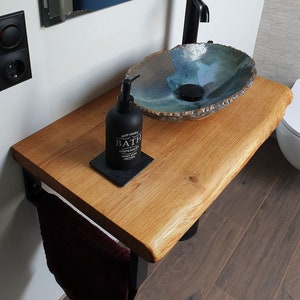 Può includere: Un mobile da bagno con un piano in legno e un portasciugamani in metallo nero. Un lavabo in ceramica blu e verde è posizionato sul piano, con un rubinetto nero e un dispenser di sapone nero etichettato "West Coast Bath Dispensers Sweet Home".