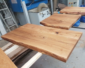 May include: Three unfinished wooden tabletops with live edges. The tabletops are made of light brown wood with a natural grain pattern. The tabletops are stacked on top of each other, with the largest tabletop on the bottom and the smallest tabletop on top.