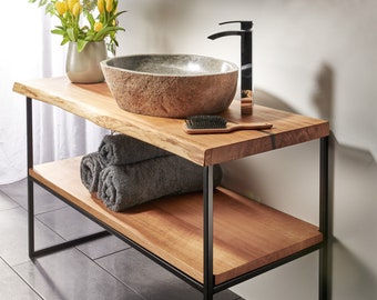 Puede incluir: Un tocador de baño de madera con un marco de metal negro. El tocador tiene un solo estante y un lavabo de piedra. Un cepillo para el cabello y toallas están en el estante.