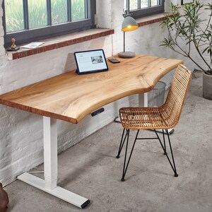 Peut inclure: Un bureau debout blanc avec un plateau en bois naturel. Le bureau a un bord incurvé et une base blanche. Un ordinateur portable est sur le bureau, et une chaise avec un siège tissé est devant le bureau.