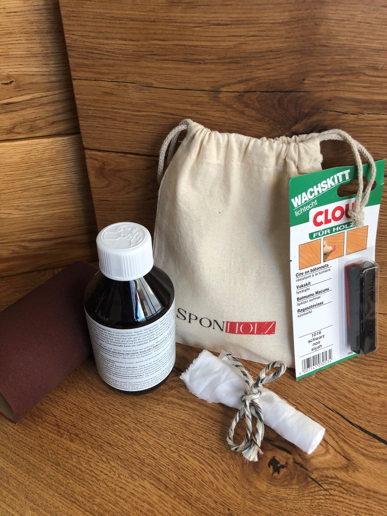 May include: A wood care kit with a brown bottle of wood polish, a white cloth, a small bag, and a black applicator. The packaging includes the text "Wachskitt lichtecht CLO F&Uuml;R HOLZ" and "SPONTOLZ".