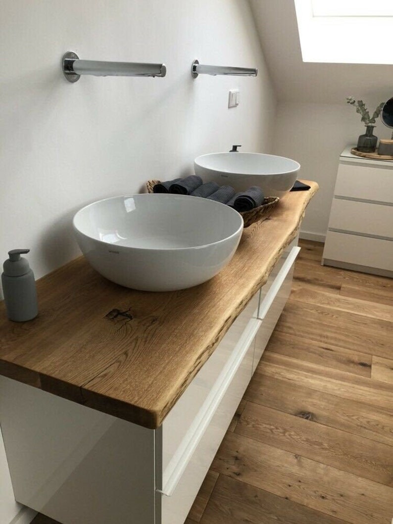 May include: White bathroom vanity with two white porcelain sinks, a wooden countertop, and white drawers. The countertop is a live edge slab of wood.