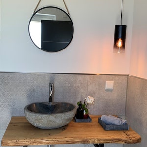 May include: A bathroom vanity with a stone sink, wooden countertop, and a round mirror hanging above. A black pendant light hangs from the ceiling.