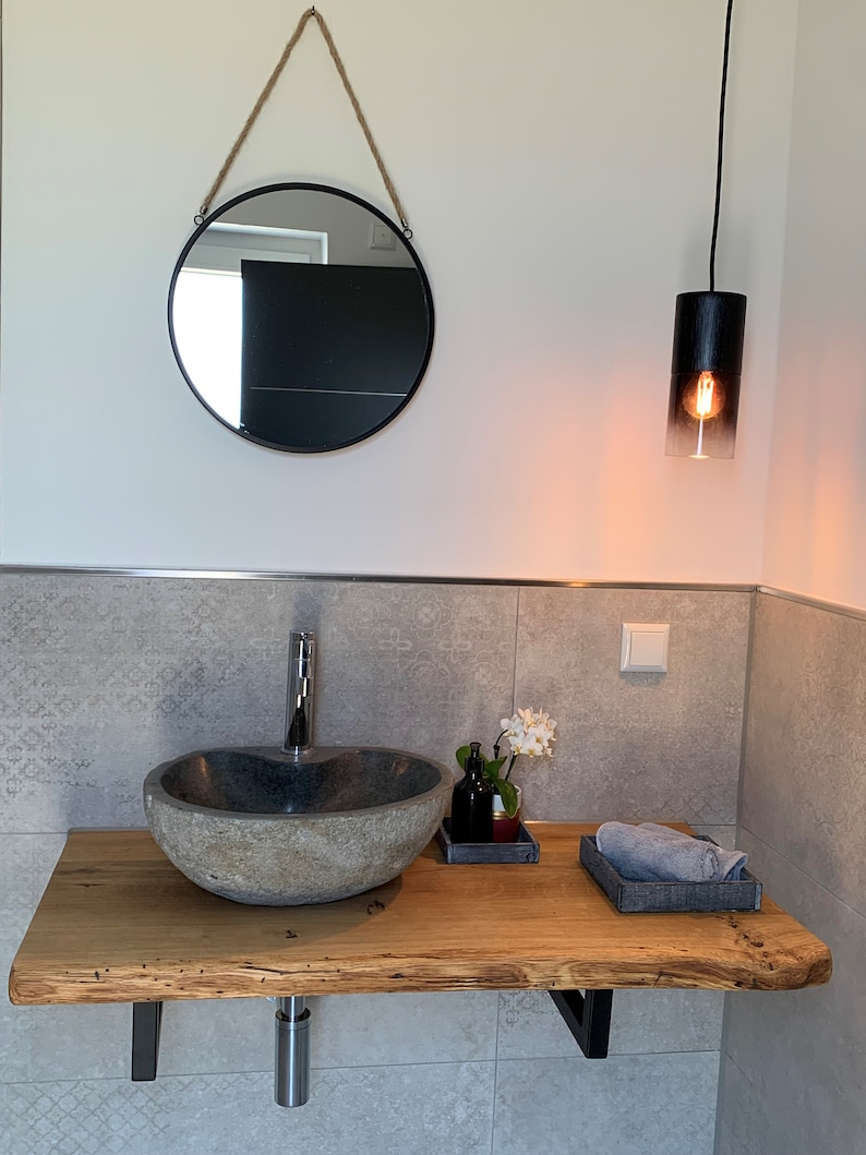 May include: A bathroom vanity with a stone sink, wooden countertop, and a round mirror hanging above. A black pendant light hangs from the ceiling.