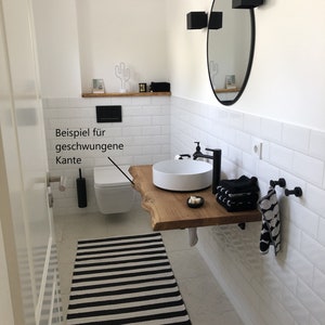 May include: A white bathroom with white subway tile walls, a black and white striped rug, a white toilet, a white sink with a wooden countertop, and a round black mirror with black sconces.