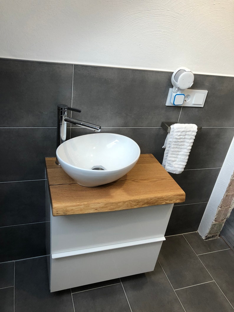 May include: White bathroom vanity with a wooden countertop and a white porcelain sink. A chrome faucet is attached to the sink. A white towel is hanging on a chrome towel rack.