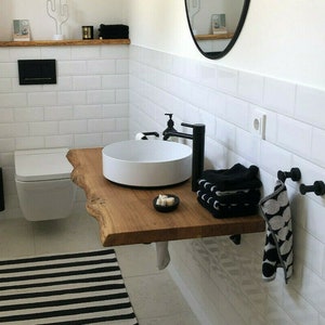 May include: A white porcelain sink with a black faucet mounted on a wooden countertop. The countertop is a natural edge slab with a live edge. Black towels are folded on the countertop and a black and white patterned towel hangs on a hook.