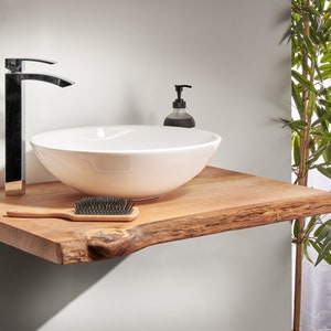 May include: A white ceramic vessel sink with a black faucet sits on a wooden countertop with a live edge. A small bottle of soap is next to the sink.