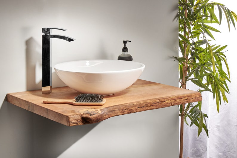 May include: A white ceramic vessel sink with a black faucet sits on a wooden countertop with a live edge. A small bottle of soap is next to the sink.