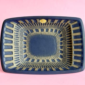 May include: A blue ceramic dish with a gold geometric pattern. The dish has a square shape with rounded corners.