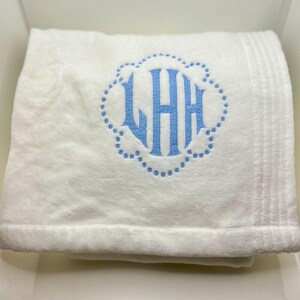 May include: A folded white towel with a light blue monogram. The monogram features the letters LHH inside a scalloped border. The towel has a plush texture and a ribbed border.
