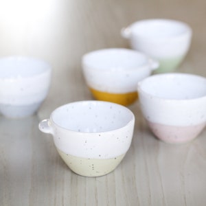 May include: Set of five small ceramic bowls with speckled white glaze and colored rims. The bowls are in shades of yellow, blue, green, and pink.
