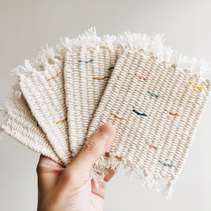 May include: Set of six woven coasters with a fringed edge. The coasters are made of natural colored fabric with colorful woven accents.