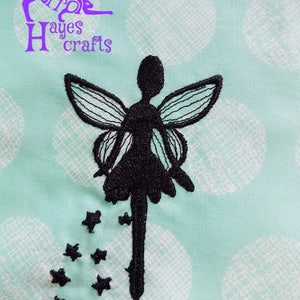 May include: Black embroidered fairy with wings and a flowing skirt, surrounded by small black stars on a light blue background with white polka dots.