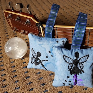 May include: Two blue fabric sachets with embroidered black fairy silhouettes and silver glitter stars. Each sachet has a blue and green tartan ribbon attached.