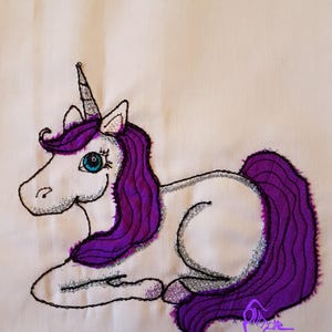 May include: White unicorn with a purple mane and tail, embroidered on a white fabric. The unicorn has a silver horn and blue eyes. The fabric has a subtle sparkle.
