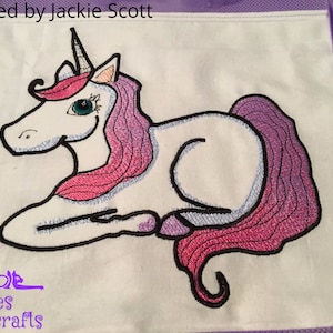 May include: Embroidered design of a white unicorn with pink and purple mane and tail, lying down on a white background. The text "Stitched by Jackie Scott" is at the top of the image.