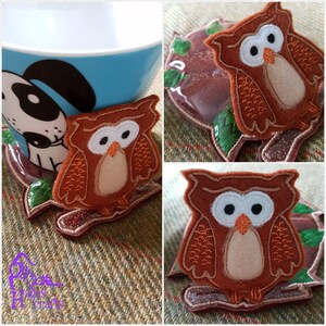 May include: Three brown owl-shaped coasters with white eyes and beaks. The owls are sitting on a branch with green leaves. The coasters are made of felt and are perfect for protecting your furniture from hot mugs and glasses.