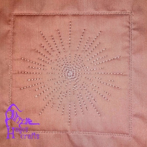 May include: A close-up of a brown fabric square with a white stitched starburst design in the centre. The fabric is textured and has a subtle sheen.