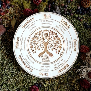May include: A wooden circle featuring a Celtic tree of life design, with the eight sabbats of the Wheel of the Year inscribed around it. The sabbats are: Yule, Imbolc, Ostara, Beltane, Litha, Lughnasadh, Mabon, and Samhain.