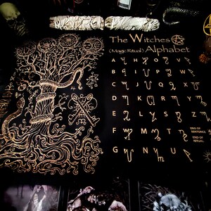 May include: A black and gold illustrated book with a tree of life design on the left page and a witches alphabet on the right page. The alphabet is written in gold and includes the text "The Witches (Magic Ritual) Alphabet".