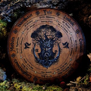 May include: A wooden wheel with a tree of life design and the names of the eight sabbats of the Wheel of the Year in French and English. The sabbats are: Samhain, Mabon, Lughnasadh, Litha, Beltane, Ostara, Imbolc, and Yule.