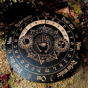 May include: A black wooden Ouija board with gold lettering and symbols. The board features the words "Oui", "Peut-être", "Non", "Reformuler", and "Retour muler".