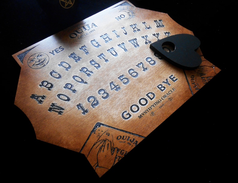 May include: A wooden Ouija board with a black heart-shaped planchette. The board features the letters of the alphabet, numbers 1-9 and 0, and the words "YES", "NO", "GOOD BYE", and "OUIJA SINCE 1891".