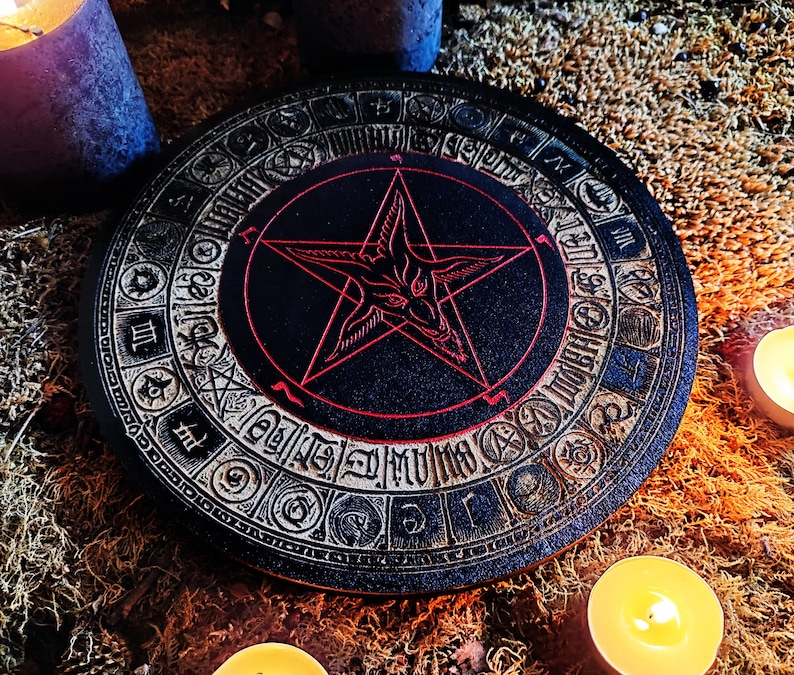 May include: A black wooden circle with a pentagram and goat's head design in red. The circle is surrounded by a ring of symbols and numbers. The circle is on a brown surface with candles.