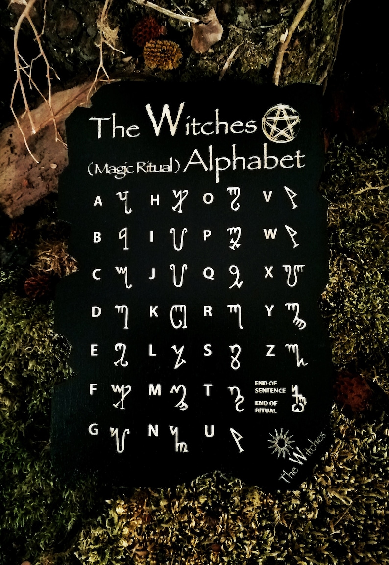 May include: Black slate board with white text and symbols. The text reads "The Witches (Magic Ritual) Alphabet". The board displays a unique alphabet with symbols for each letter. The symbols are white on a black background.